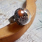 Bague Majesté Steampunk aux rouages mécaniques à laquelle s’ajoute une clé et un strass de couleur Siam et un strass en verre Doré. Le tout est mis sous un globe en verre sur une bague réglable laiton