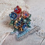 Bague Bel Air montée avec des fleurs lucites peintes à la main aux couleurs : Bleu, Rose, Rouge, Argent, Blanc avec feuilles ondulées Vert Cuivré à laquelle s’ajoute perles Dorées en Verre