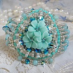Bracelet Blue Flowers Haute-Couture brodé avec des Cristaux de Swarovski, un cabochon en résine, des perles rondes en satin, des rocailles avec une chaînette et un fermoir en Argent 925/1000