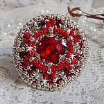 Bague Drigon Red brodée avec un cabochon carré Rouge sur une estampe Argentée. Ornée de chatons en Cristal puis modelée avec des rocailles et perles. Le tout est monté sur une bague réglable argentée 